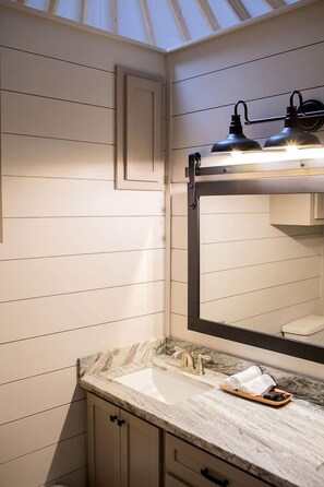 Un bany amb taulell de marbre, un lavabo, un mirall i un llum al sostre.