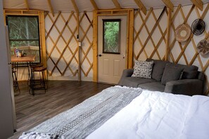 A cozy room with a bed, a sofa, a table with stools, and a door with a window.