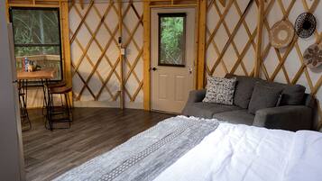 A cozy room with a bed, a sofa, a table with stools, and a door with a window.