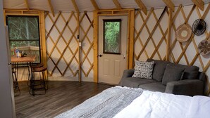 A cozy room with a bed, a sofa, a table with stools, and a door with a window. - Fully-Equipped Yurt Rental for Memorable Family Vacations in Livingston, Texas (Livingston)