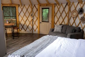 A cozy room with a bed, a sofa, a table with stools, and a door with a window.