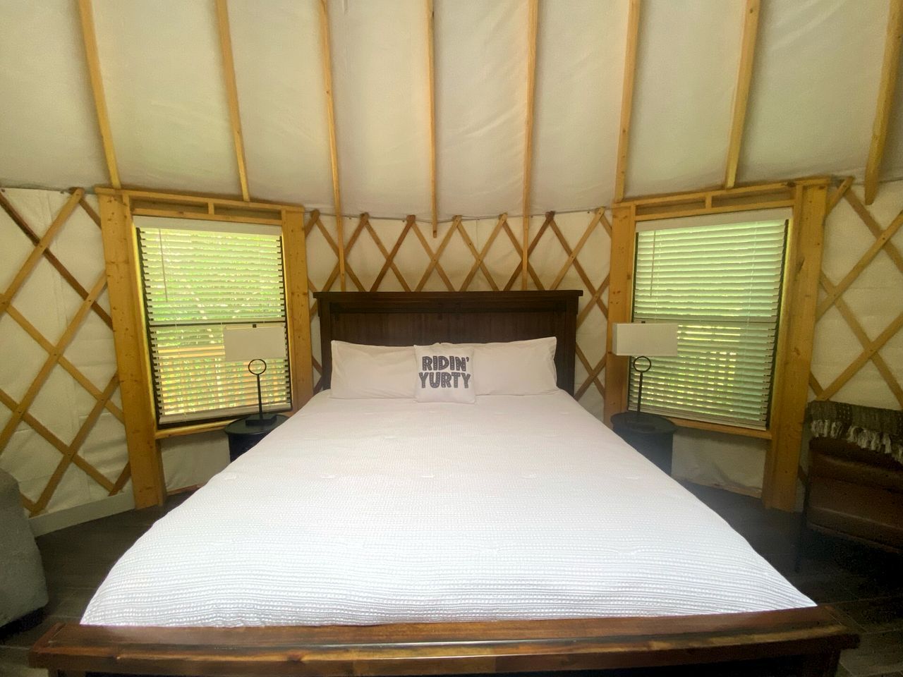A bed in a tent with a wooden headboard, two bedside tables, and a pillow with text.