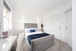 Une chambre à coucher avec un lit, des tables de chevet, une lampe, une plante en pot et une porte.