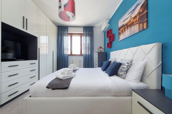 A modern bedroom with a bed, a TV, and a painting on the wall.