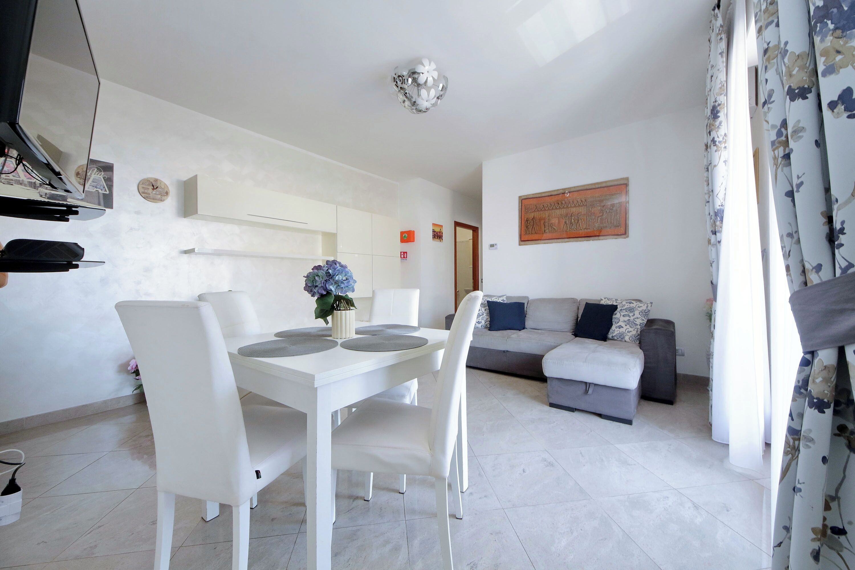 A modern living room with a dining table, chairs, a sofa, and a decorative wall piece.