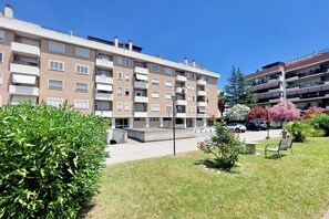Kerrostalo, jossa on useita kerroksia, parvekkeita, kivetty sisäpiha ja vehreää ympäristöä.