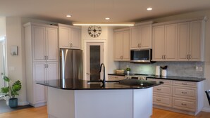 Una cocina moderna con armarios blancos, un refrigerador de acero inoxidable, un microondas y una isla grande con encimera negra.