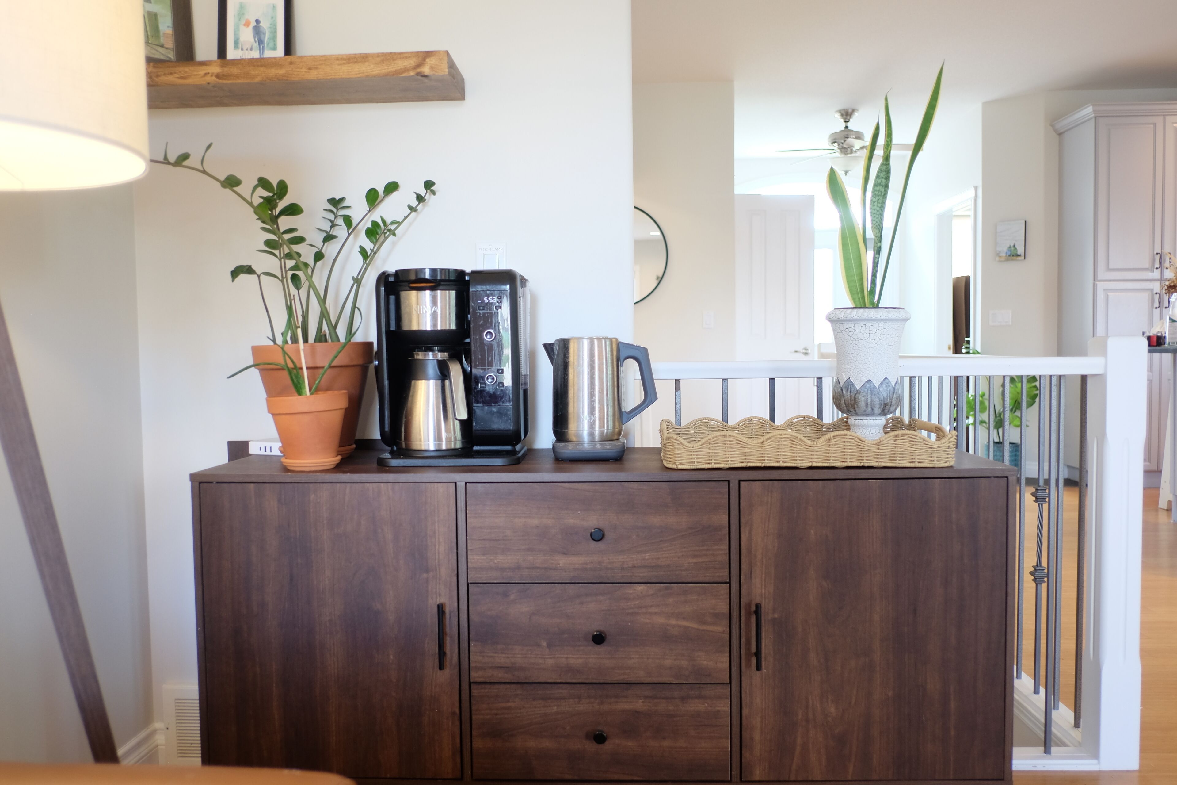 A wooden cabinet with a coffee maker, two potted plants, and a wicker basket.