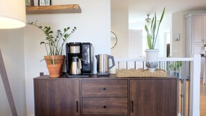 Un mueble de madera con una cafetera, dos plantas en macetas y una cesta de mimbre.
