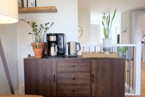 Ein Holzschrank mit Kaffeemaschine, zwei Zimmerpflanzen und einem Korbwäscher.
