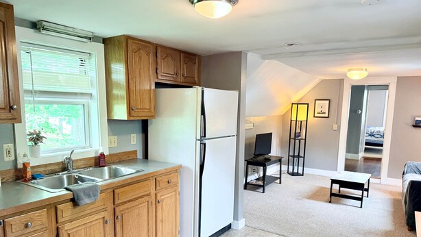 A kitchen with wooden cabinets, a refrigerator, a sink, and a window with blinds.