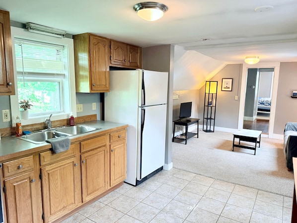 A kitchen with wooden cabinets, a refrigerator, a sink, and a window with blinds.