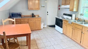 A compact kitchen with wooden cabinets, a microwave, a stove, and a dining table with chairs.