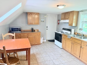 A compact kitchen with wooden cabinets, a microwave, a stove, and a dining table with chairs.