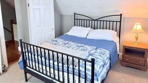 A bedroom with a bed, a nightstand, a lamp, a door, and a staircase.