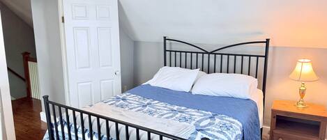 Une chambre à coucher avec un lit, une table de chevet, une lampe, une porte et un escalier.