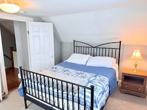 A bedroom with a bed, a nightstand, a lamp, a door, and a staircase.