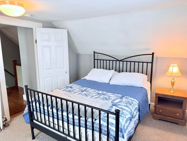 A bedroom with a bed, a nightstand, a lamp, a door, and a staircase.