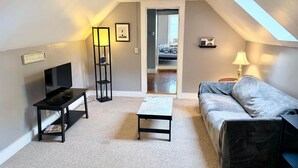 A compact living space with a sofa, a coffee table, a TV on a stand, a floor lamp, and a bookshelf.