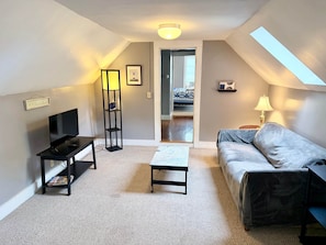A compact living space with a sofa, a coffee table, a TV on a stand, a floor lamp, and a bookshelf.