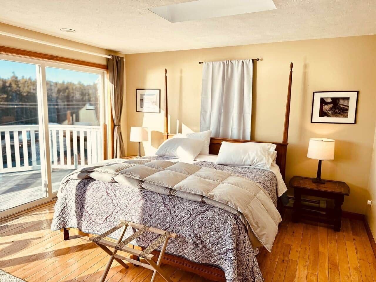 Een slaapkamer met een groot bed, een houten vloer, een balkon en een nachtkastje met een lamp.