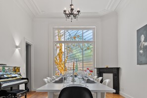 A dining room with a piano, a stained glass window, and a fireplace.
