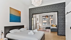 A modern bedroom with a large bed, a painting, and a view into the living area. - Grand Ostend townhouse with sauna near the sea (Oostende)