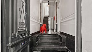 A hallway with a black and white checkered floor, a red statue, and a staircase leading to a door with a circular window. - Grand Ostend townhouse with sauna near the sea (Oostende)