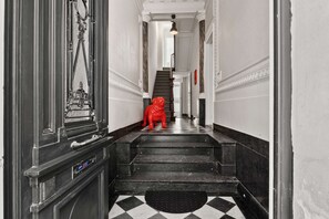Ein Flur mit einem schwarz-weißen Schachfußboden, einer roten Statue und einer Treppe, die zu einer Tür mit einem runden Fenster führt.