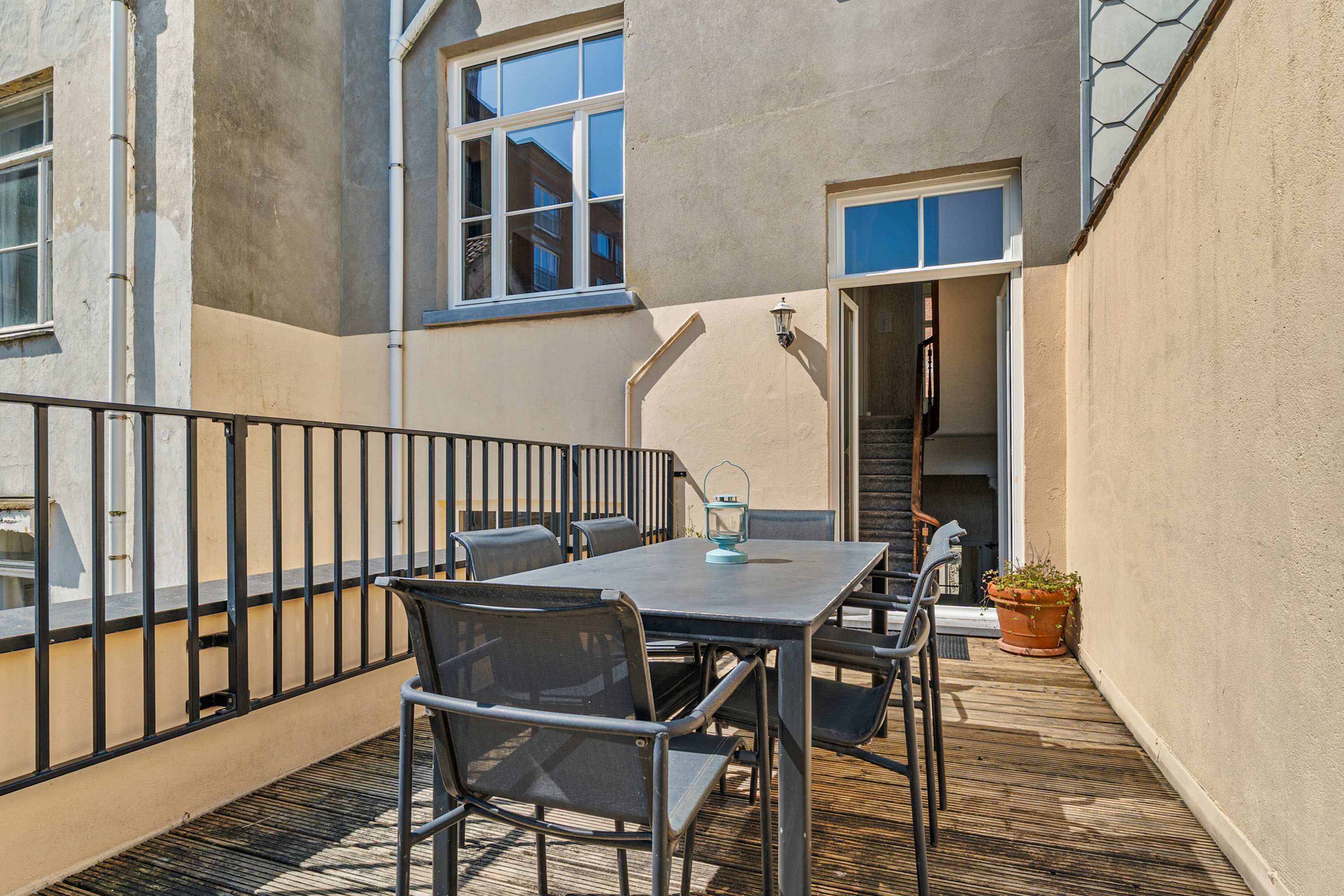 Un balcon avec une table et des chaises, une plante en pot et une vue sur l’intérieur du bâtiment.