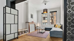 A modern living room with a sofa, a table, a bookshelf, and a decorative hanging light fixture. - Grand Ostend townhouse with sauna near the sea (Oostende)