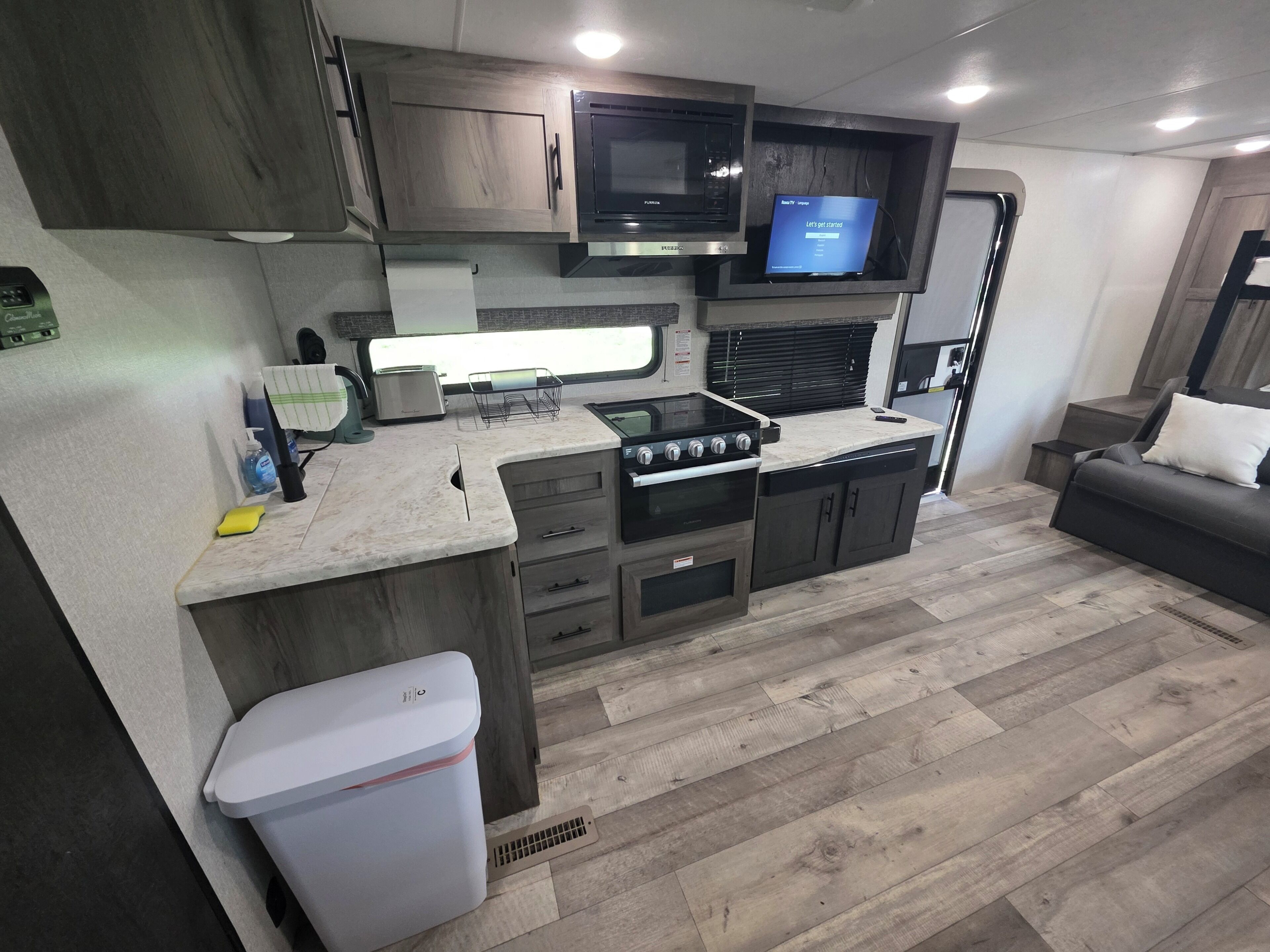 A compact kitchen with a stove, microwave, and a flat-screen TV.