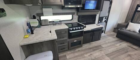 A compact kitchen with a stove, microwave, and a flat-screen TV.
