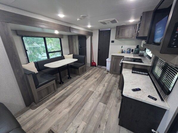 Une cuisine moderne pour camping-car, avec un coin repas, un plancher en bois et des appareils électroménagers intégrés.