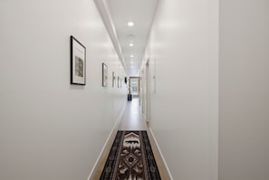 Un couloir aux murs ornés de tableaux encadrés, un tapis à motifs et un plafond doté d’un éclairage encastré.