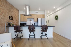 A modern kitchen with a brick wall, wooden cabinets, a stainless steel range hood, and a bar area with stools.