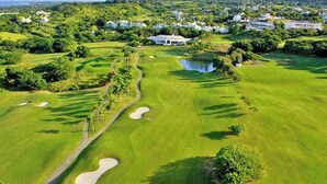 Un campo de golf con búnkeres de arena, un estanque y un edificio blanco al fondo.