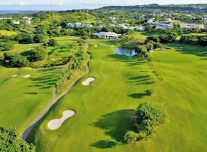 Ein Golfplatz mit Sandbunkern, einem Teich und einem weißen Gebäude im Hintergrund.
