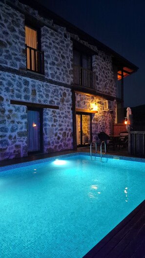 A stone building with a swimming pool, a wooden deck, and a balcony.