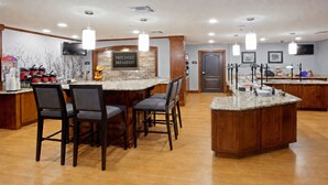 A hotel breakfast area with a sign for free daily breakfast, a TV mounted on the wall, and a counter with various breakfast items.