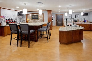 A hotel breakfast area with a sign for free daily breakfast, a TV mounted on the wall, and a counter with various breakfast items.
