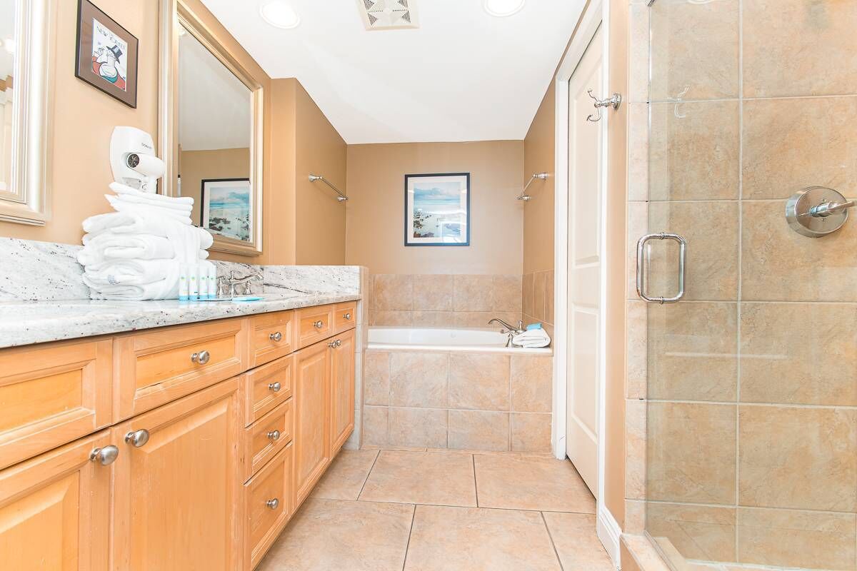 Un baño moderno con encimera de mármol, armarios de madera, bañera y zona de ducha.