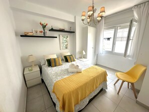 A bedroom with a bed, bedside tables, a chair, a window, and a chandelier. - R1400 Edif. Sirena 2F (Nerja)