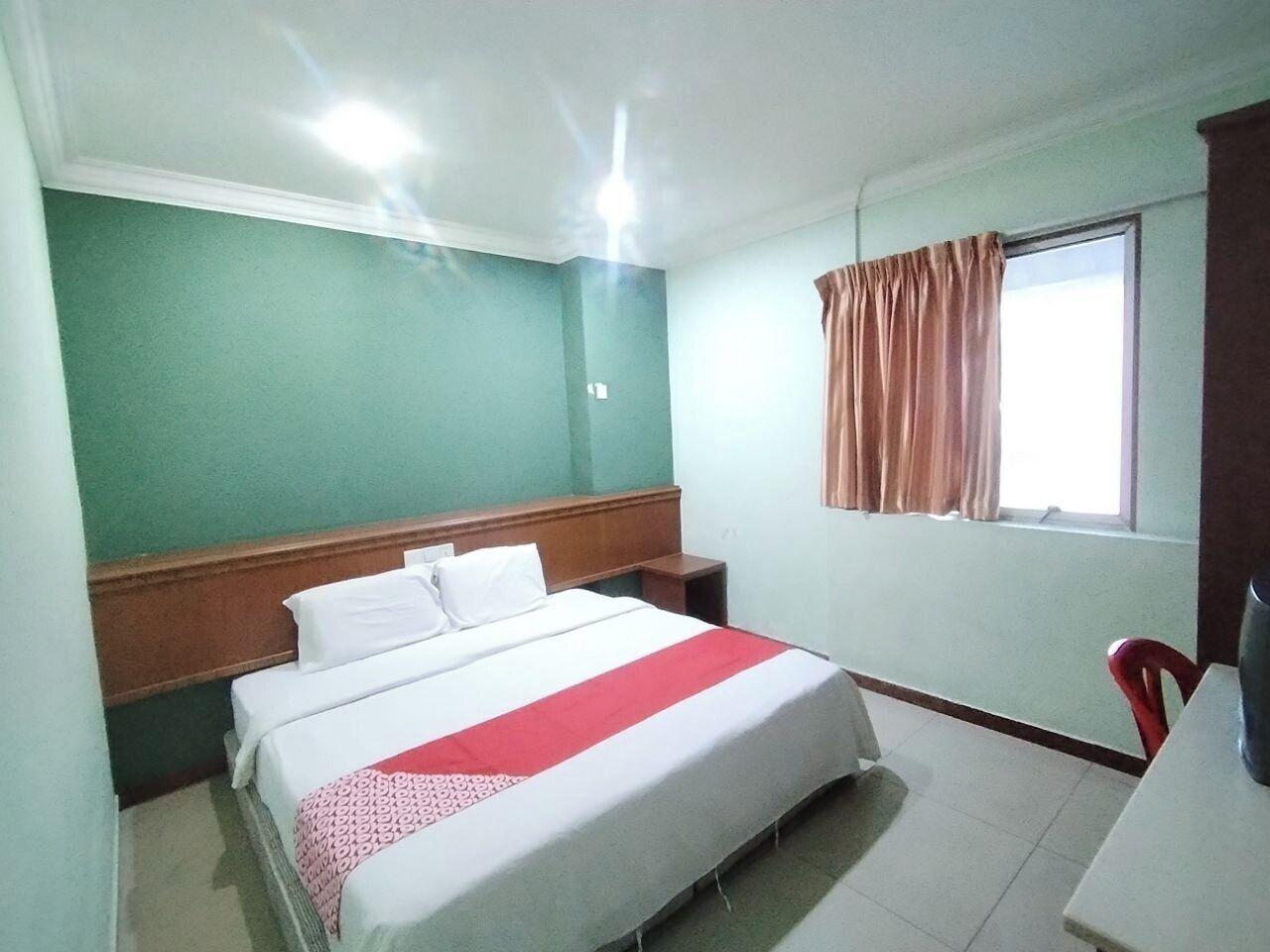 A hotel room with a bed, a desk, a window with curtains, and a green wall.