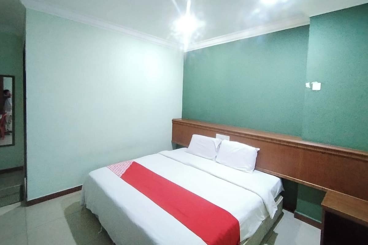 Een hotelkamer met een bed, een houten hoofdeinde, een nachtkastje en een groene wand.