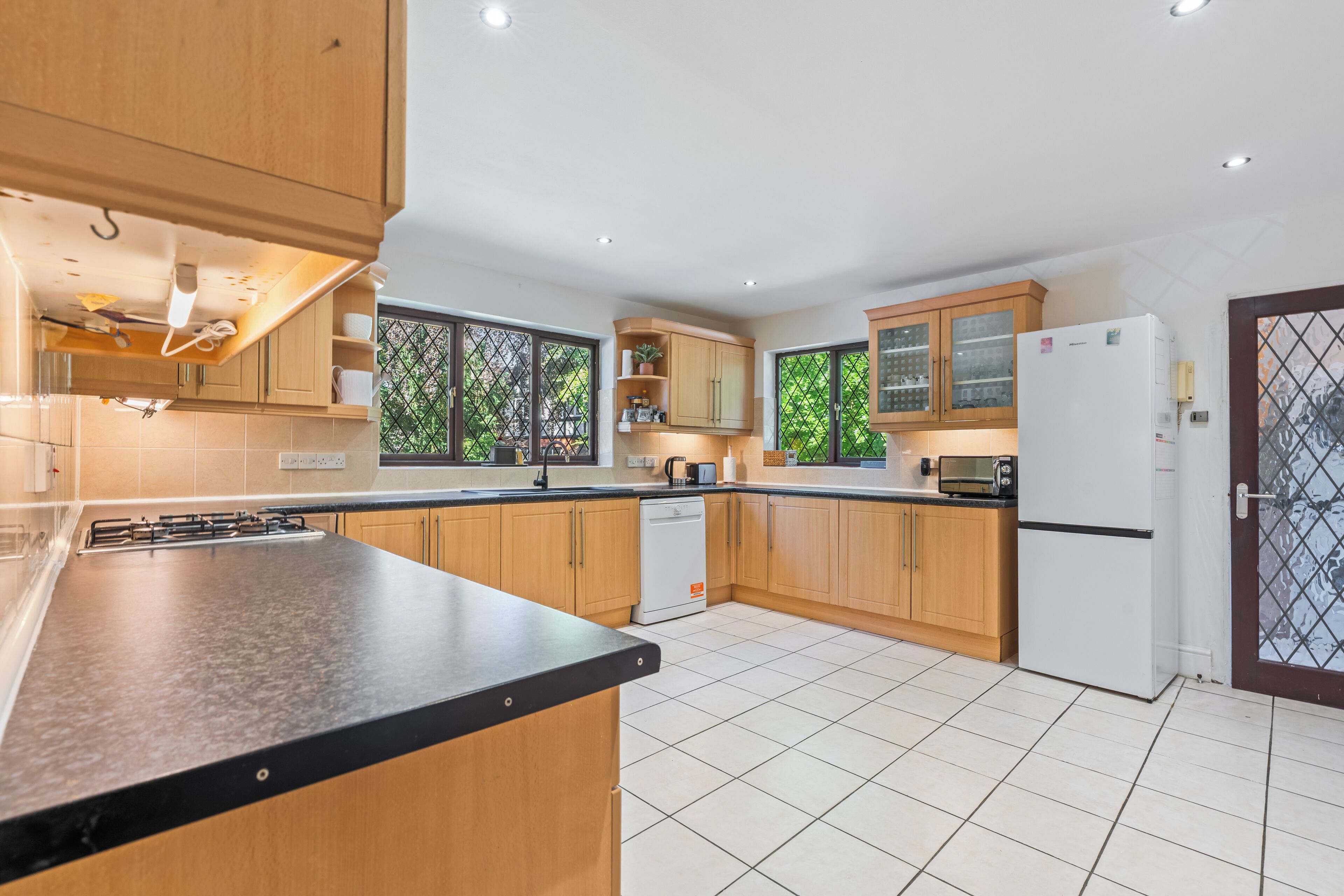 Una cocina moderna con armarios de madera, encimera negra, lavavajillas, refrigerador y ventana con vistas a la vegetación.