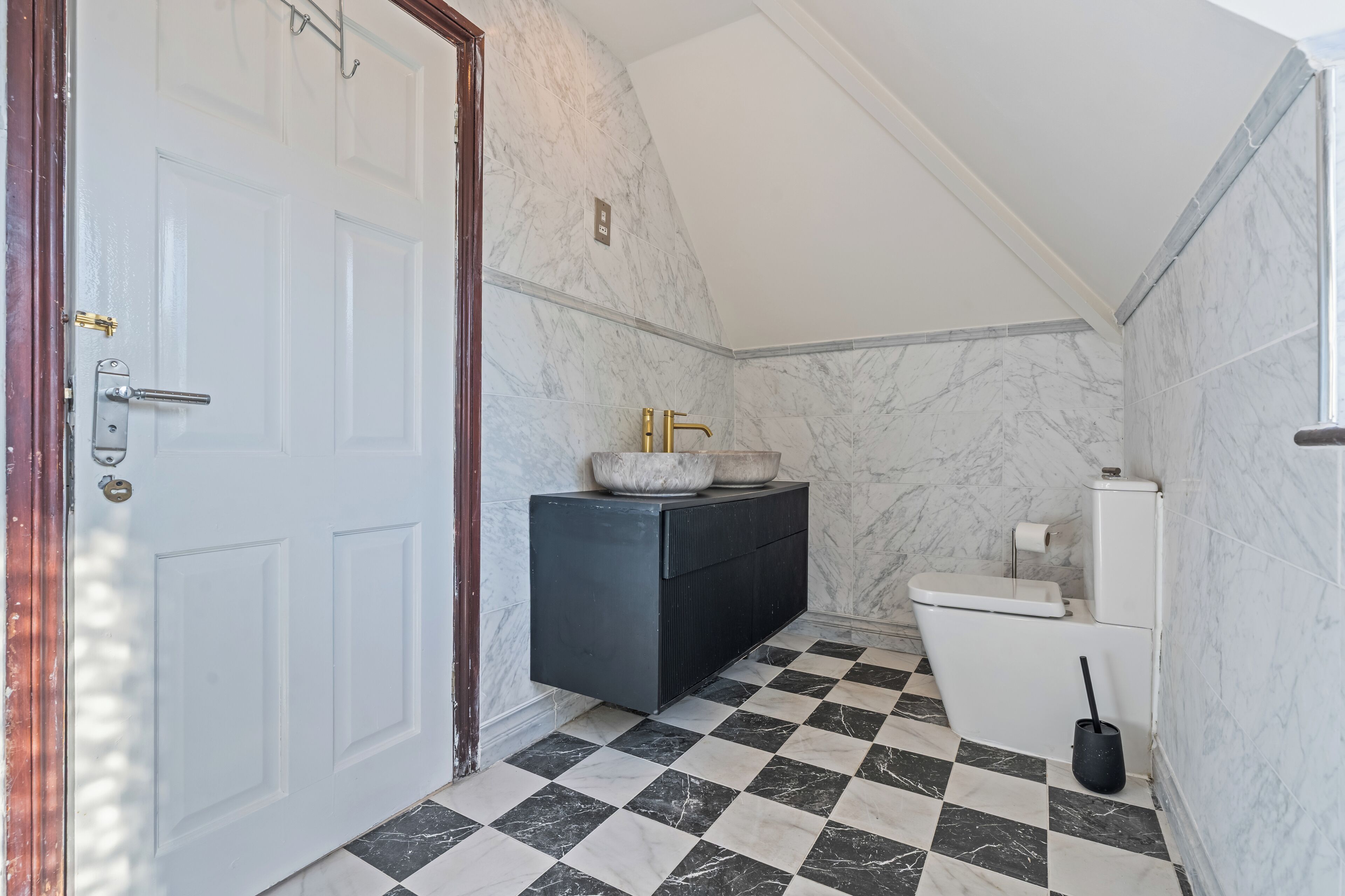 Une salle de bain avec un carrelage à motifs géométriques, une porte blanche, un meuble noir et des toilettes.
