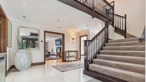 Ein geräumiges Foyer mit einem polierten Boden, einer großen Dekovase, einer Treppe mit dunkler Geländer und einem Fernseher im Hintergrund.