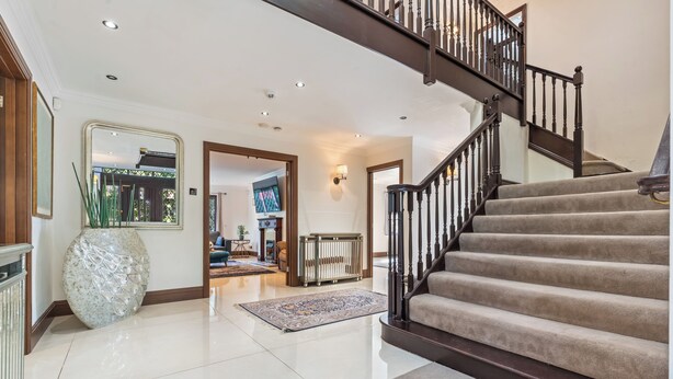 A spacious foyer with a polished floor, a large decorative vase, a staircase with a dark railing, and a television in the background. - Family 6 Bed | Gated Parking, Sleeps 11, Bray (Bray)