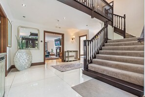 A spacious foyer with a polished floor, a large decorative vase, a staircase with a dark railing, and a television in the background. - Family 6 Bed | Gated Parking, Sleeps 11, Bray (Bray)